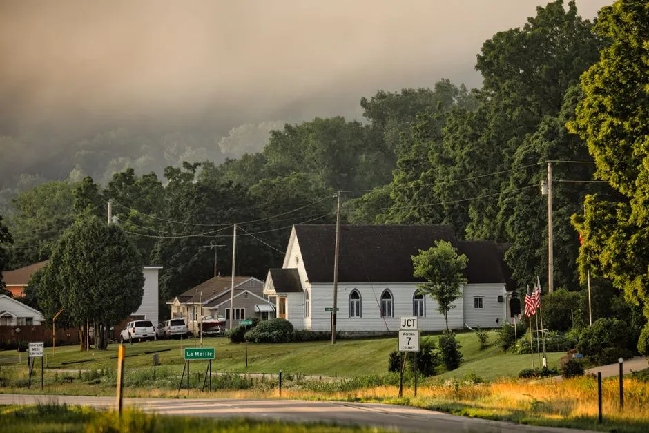 Houses and a small church along a rural road, surrounded by trees